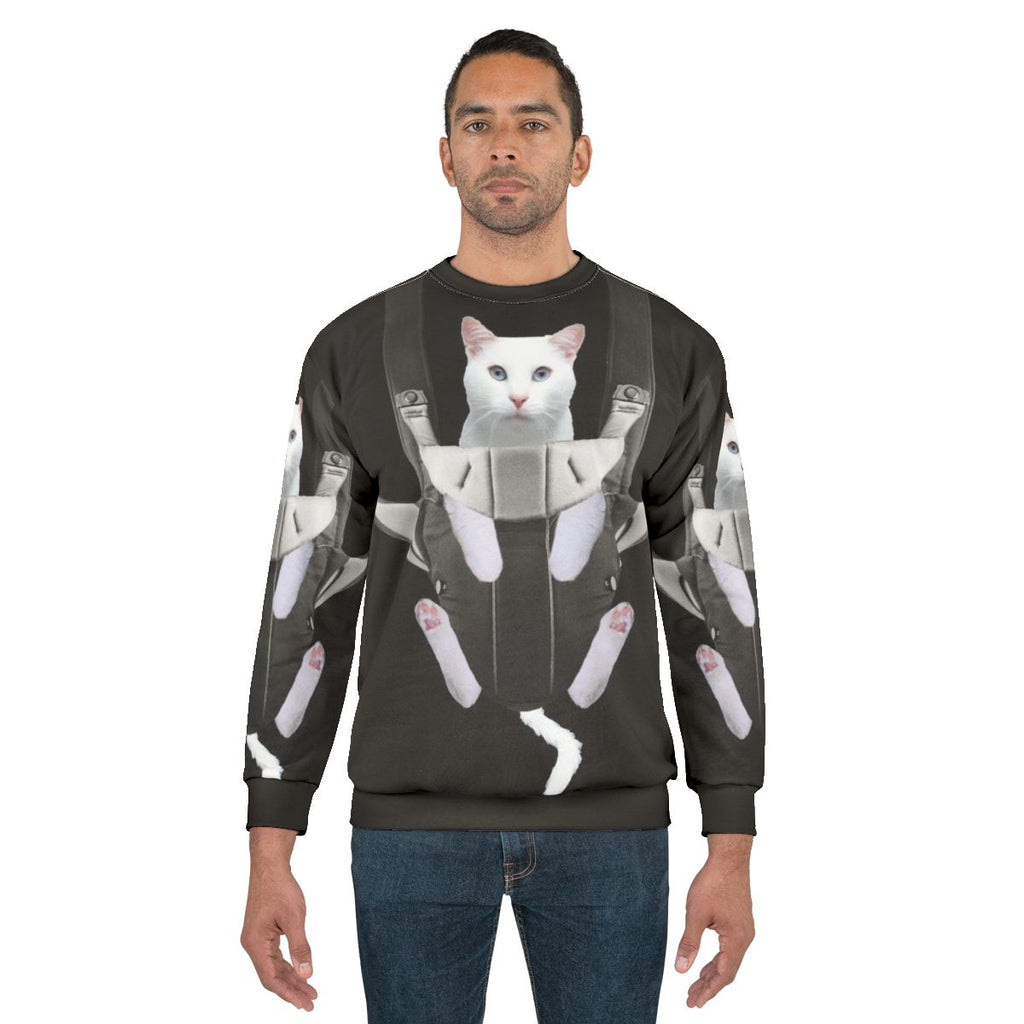 Tabby cat snuggling in a baby carrier on a white sweatshirt