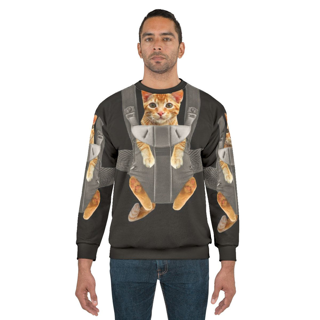Monty the cat wearing a baby carrier on a sweatshirt