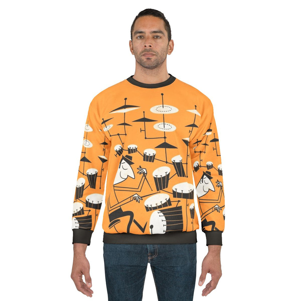 A person wearing a sweatshirt with a graphic design of drums and the text "Play That Beat"