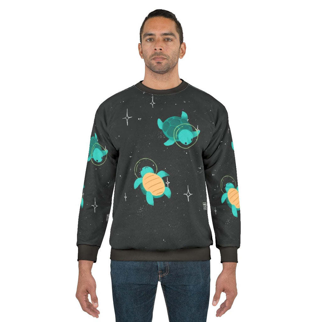 A sweatshirt featuring a playful space turtle design with stars and planets