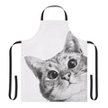 A black and white cat peeking out from behind a funny cat-themed kitchen apron