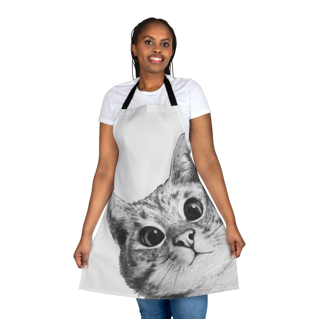 A black and white cat peeking out from behind a funny cat-themed kitchen apron