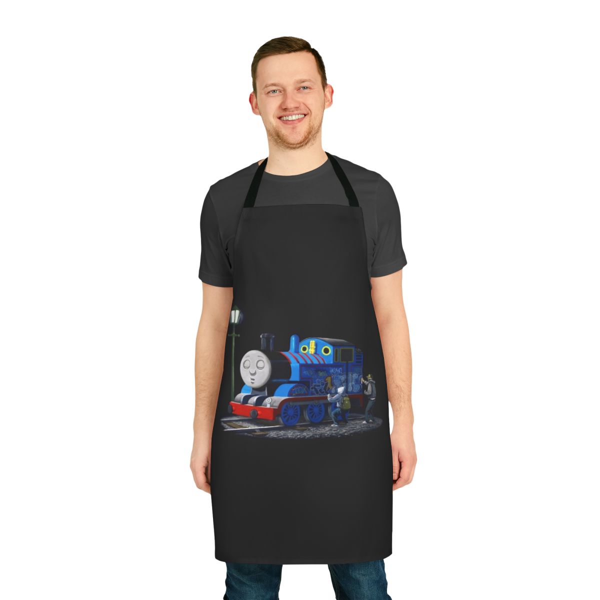 A black and white apron featuring a Banksy-style stencil graffiti design of Thomas the Tank Engine, a popular cartoon character.