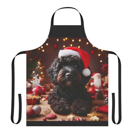 A black cockapoo dog wearing a Santa hat on a Christmas-themed apron