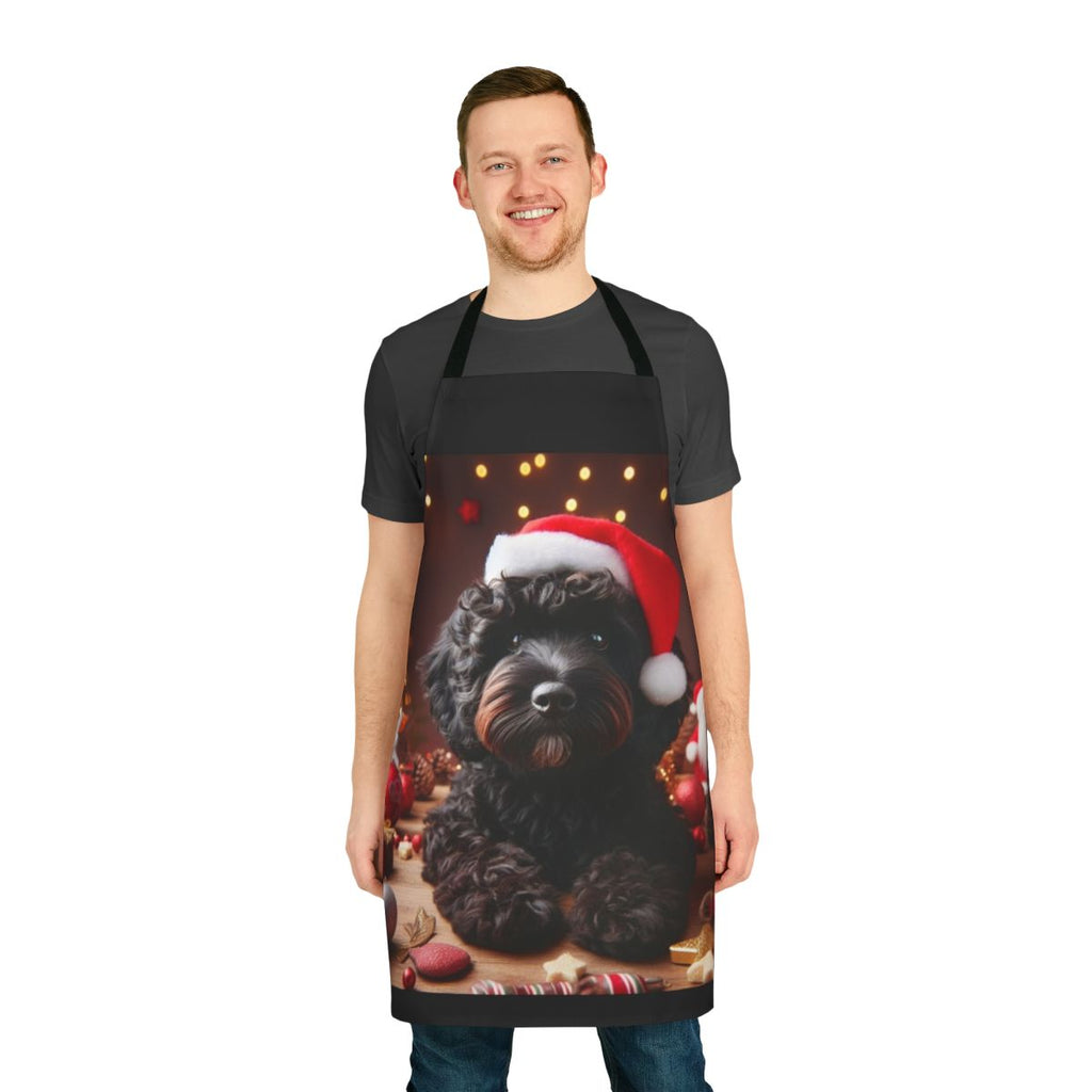 A black cockapoo dog wearing a Santa hat on a Christmas-themed apron