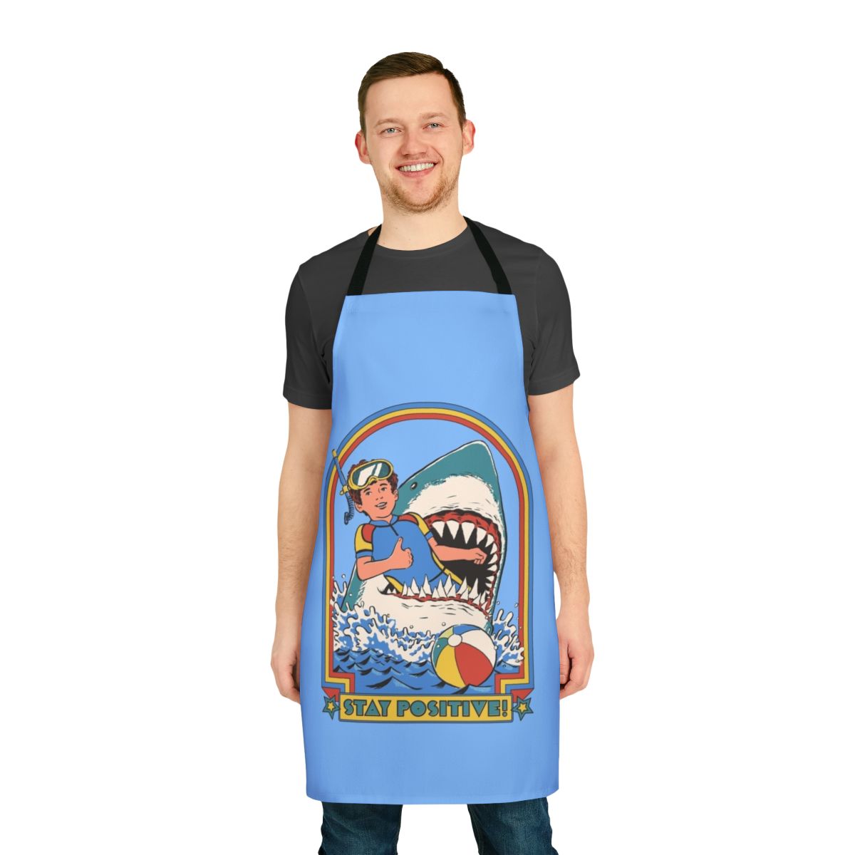 A white apron with a vintage-style illustration of a shark swimming in the ocean, with the text "Stay Positive" printed on it.
