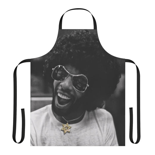 Black and white photo of a musician wearing a kitchen apron with a star of David and gold and diamond accents, in a recording studio.